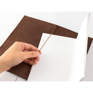 Brown leather traveler's notebook with open cover as a hand inserts paper.