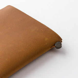 Camel-brown notebook corner close-up with metal button and leather cover texture