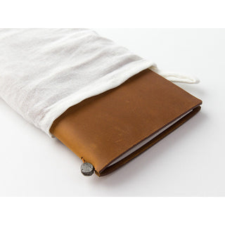 Camel-brown leather notebook wrapped in a white cotton bag with metal button closure