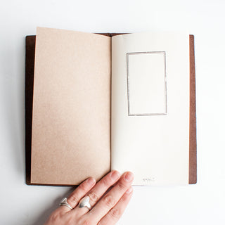 Brown leather traveler's notebook opened with blank inner pages and a pocket.