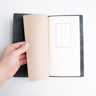 Black notebook opened with blank pages and beige insert sheet