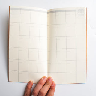 Open dated monthly planner notebook with blank grid pages and tan page edges