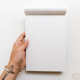 Grid notepad with white pages and light gray graph lines, held by hand at left