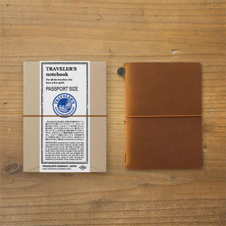 Passport-size leather notebook in camel brown with band closure and travel label insert
