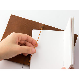 Hand inserting a sheet into a camel brown leather notebook sleeve