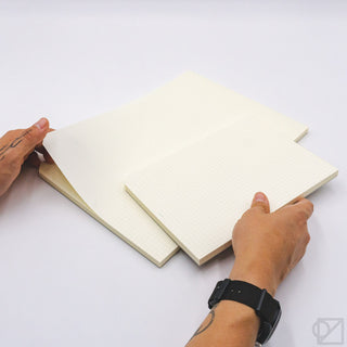 Cream grid paper pads being opened, with hands lifting a sheet from the cover.