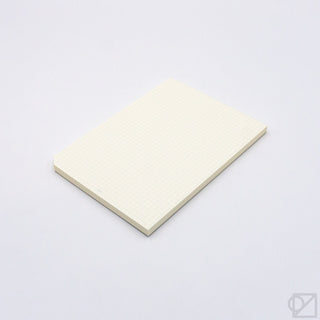 Cream graph paper pad with fine grid pattern, closed and stacked neatly.