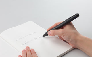 Black 4Functions pen held in hand, writing over lined paper