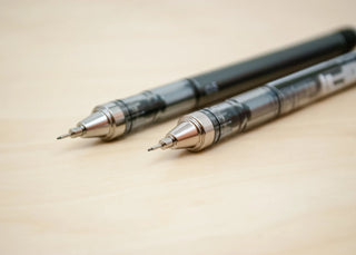 Two blue and black mechanical pencils side by side on a light wood surface