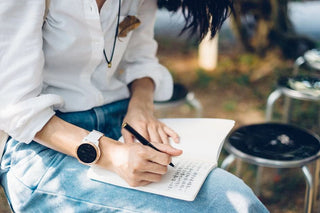 Person writing with a black ballpoint pen on an open notebook outdoors